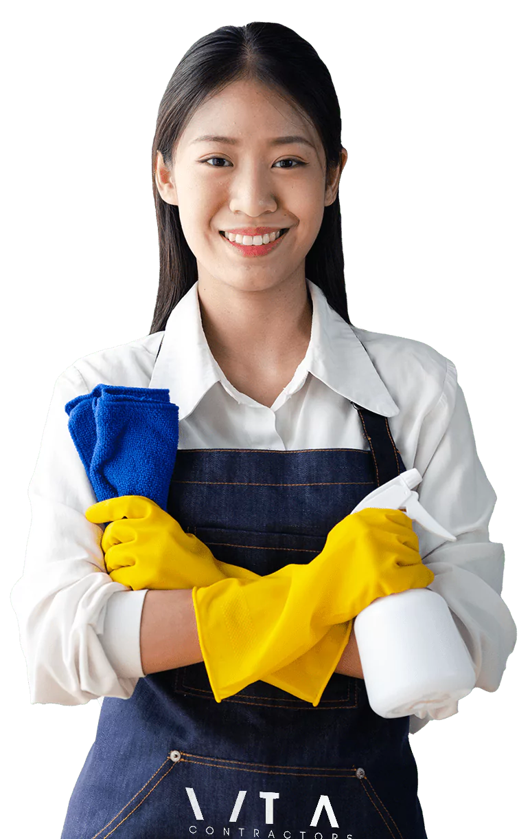 Smiling female cleaner wearing yellow gloves and VIA Contractors apron, holding a blue cloth and spray bottle.